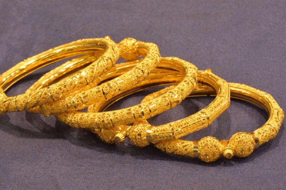 Four ornate gold kada bangles laid out on a grey cloth at Lakshmis Jewellers, East Ham